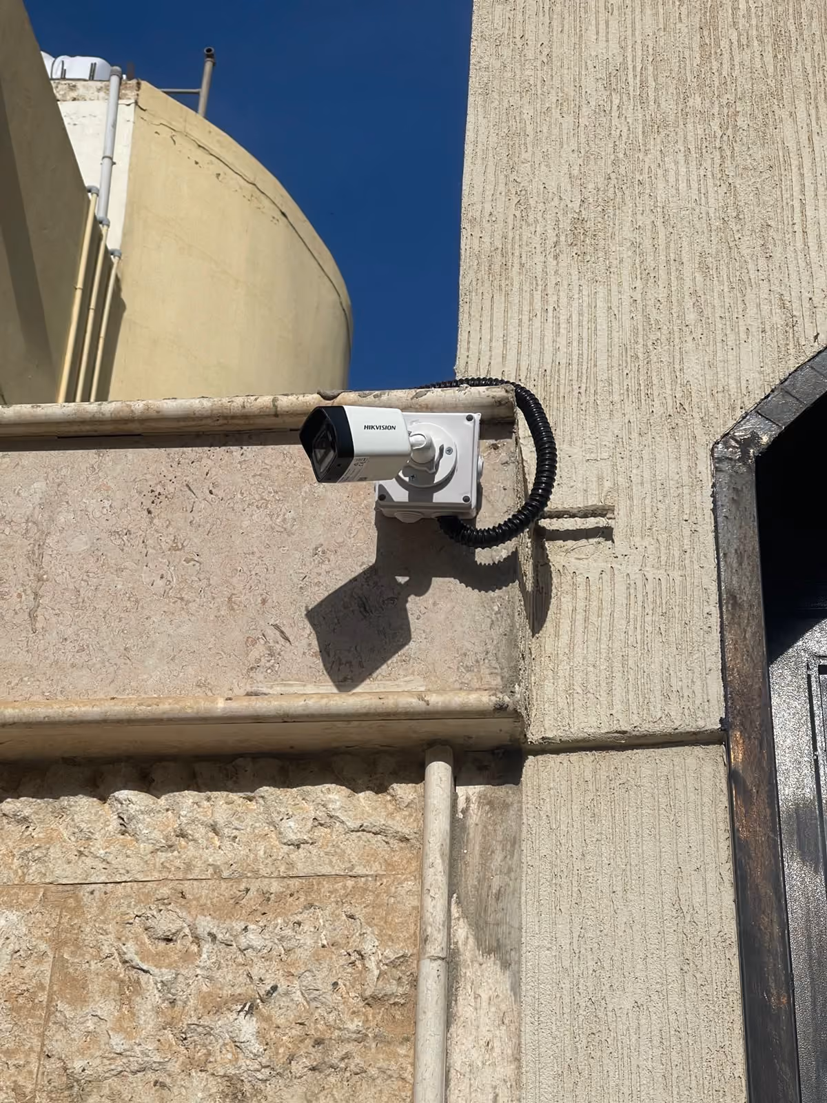 كاميرا مراقبة مثبّتة على واجهة حجرية مع ماسورة تمديد مدرّعة