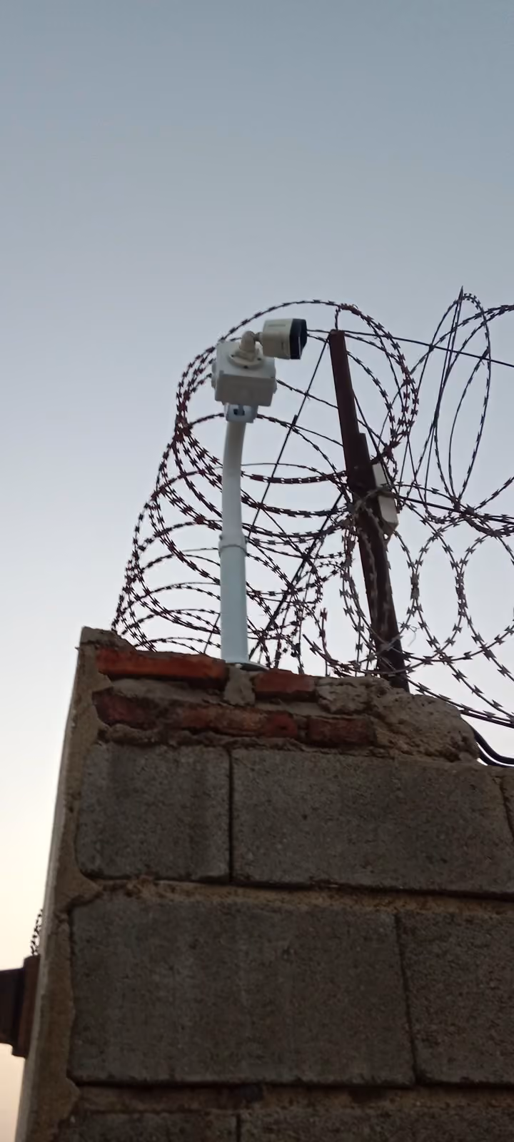كاميرا مراقبة على عمود فوق سلك شائك على سور محيط